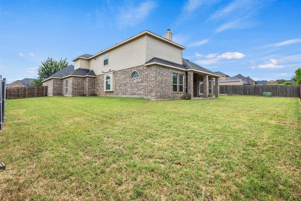 Expansive backyard featuring a manicured lawn, brick and siding exterior, covered patio, arched windows, and wood fencing