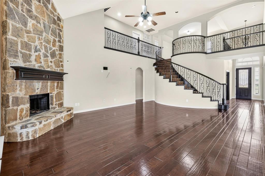 Double-height living area featuring a full-height stone masonry fireplace, wood-finish flooring, a curved staircase with ornate iron railing, and a landing overlook