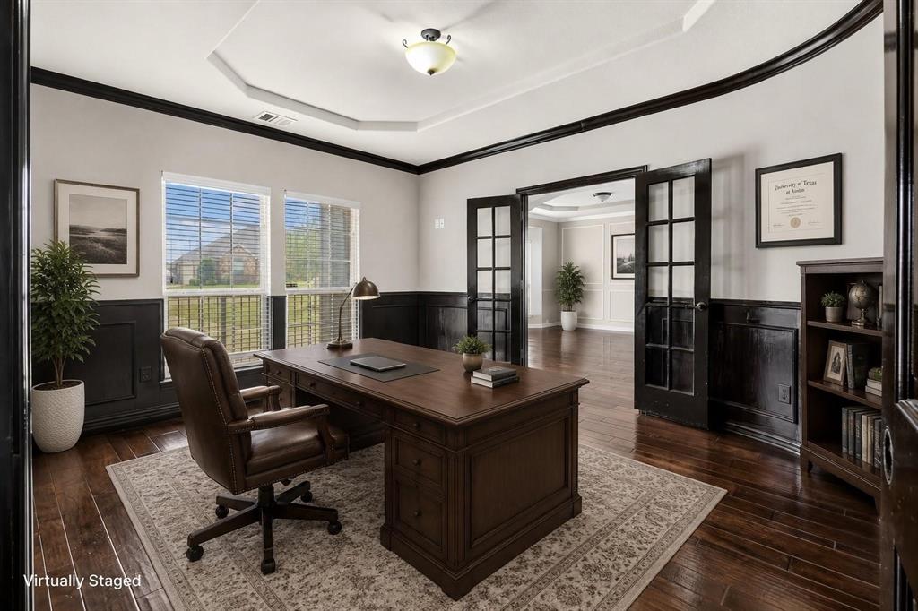 Room featuring wood-finish flooring, tray ceiling, dark-tone wainscoting, and French doors with glass panes