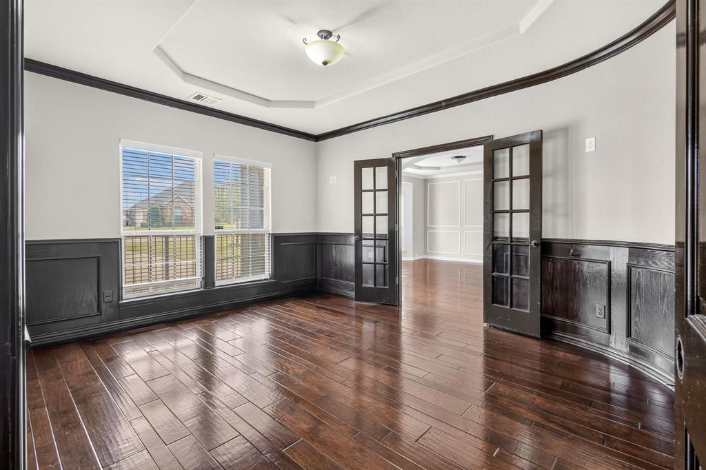 Tray ceiling, dark-stained wood-finish flooring, half-wall wainscoting, and glass-paneled French doors