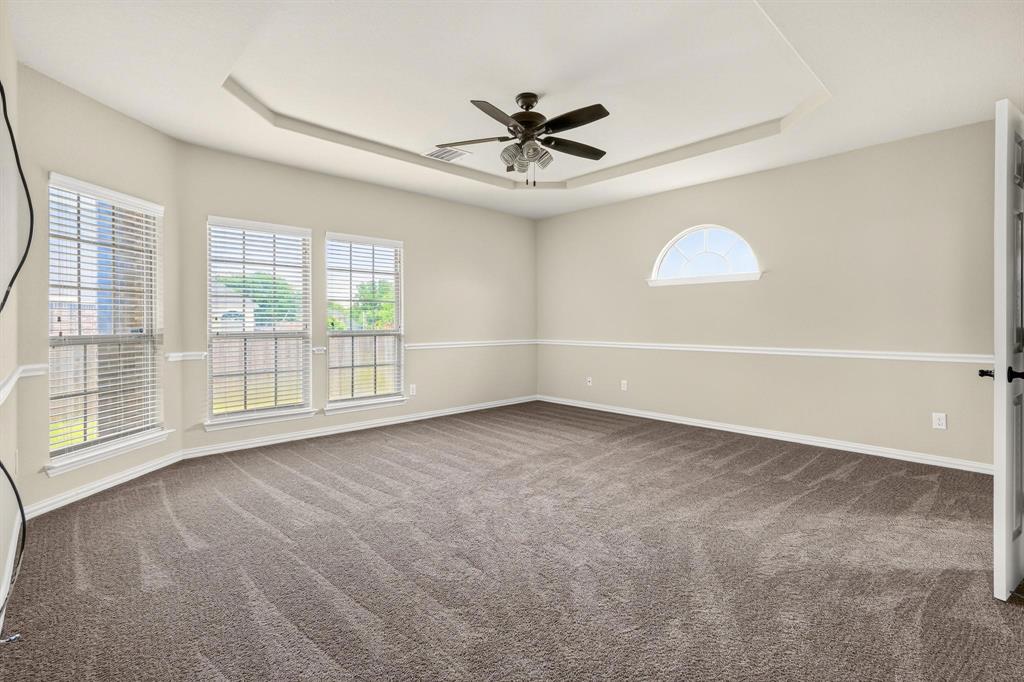 Interior room featuring a tray ceiling, ceiling fan, carpeting, windows with horizontal blinds, and a semi-circular accent window with chair rail molding