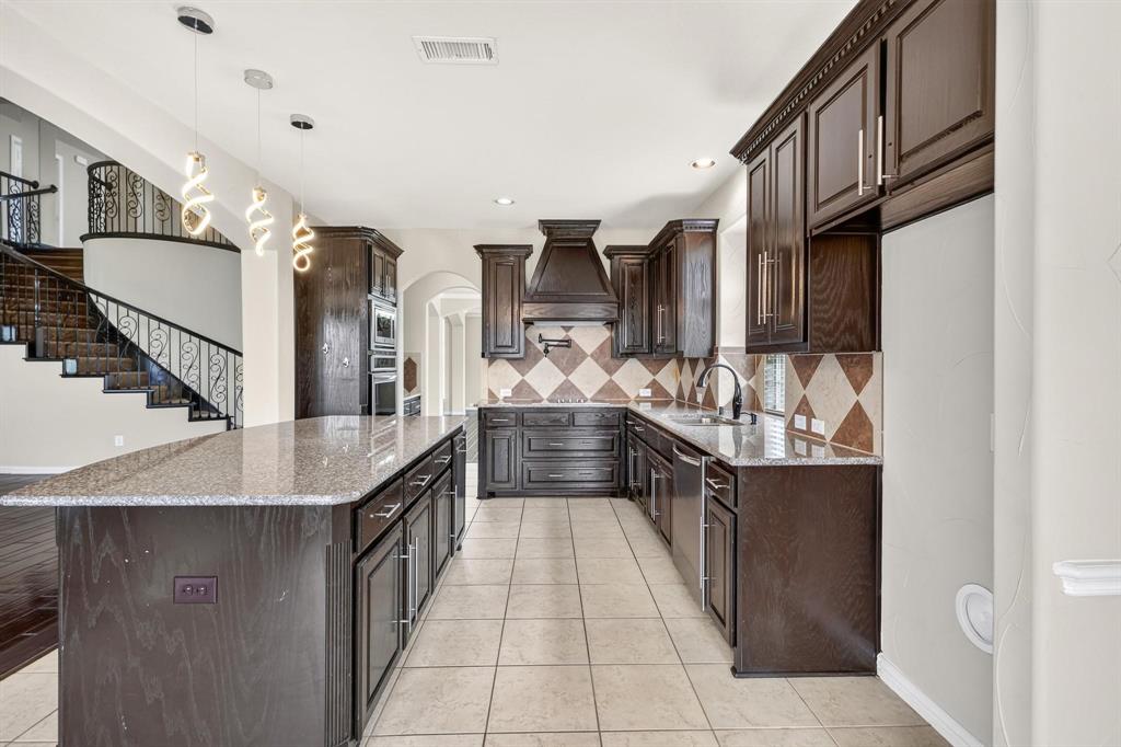 Kitchen featuring dark wood cabinetry, expansive stone-surface island, diamond-pattern tile backsplash, professional-style range hood, and pendant lighting