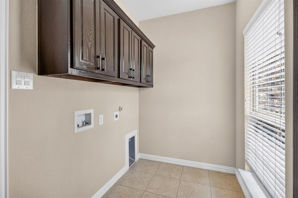 Utility area featuring dark wood-finish cabinetry, neutral tile flooring, and horizontal window blinds