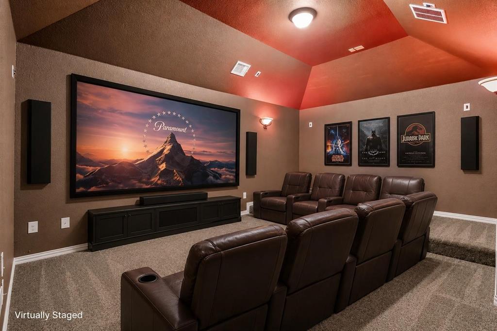 Media room featuring a vaulted ceiling, tiered platform flooring, wall-mounted sound panels, and a built-in media console
