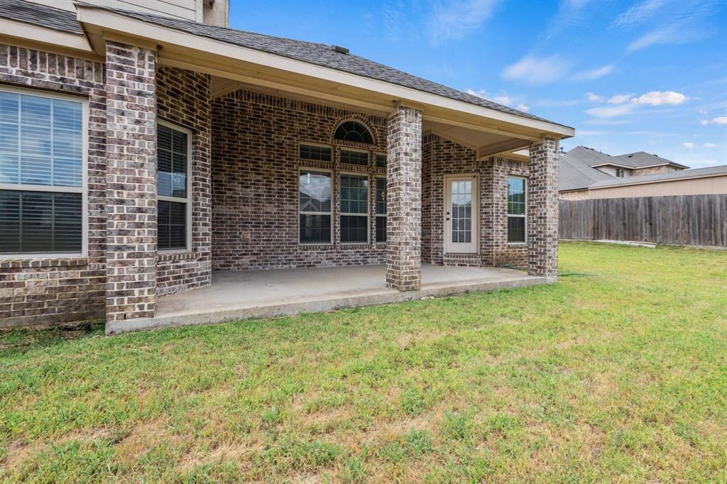 Covered concrete patio featuring brick exterior columns, arched window detailing, and an expansive lawn