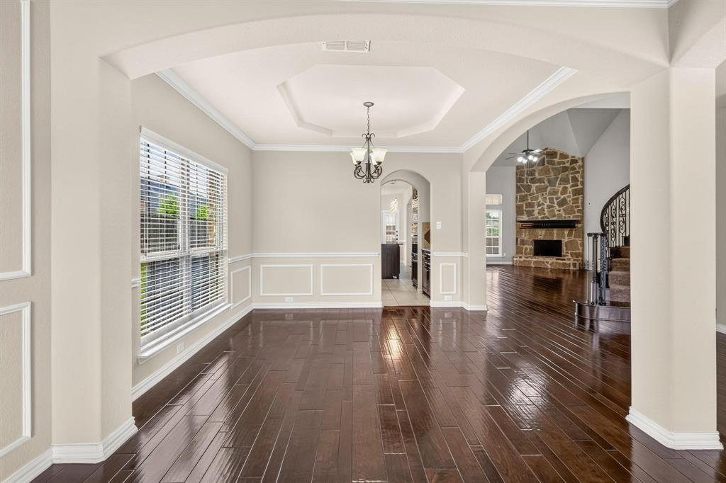 Wood-finish flooring, tray ceiling with recessed lighting, crown molding, wainscoting, and stone-surround fireplace