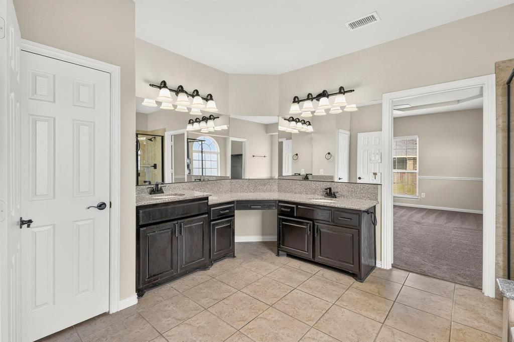 Double vanity with a central seated makeup station, stone-surfaced countertop, dual under-mount sinks, dark-finish cabinetry, and multi-bulb vanity lighting