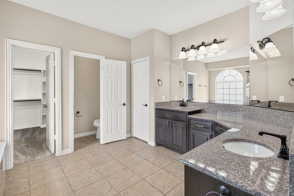 Bathroom featuring dark-finish cabinetry, stone-surface countertops, dual undermount sinks with matte black faucets, and ceramic tile flooring
