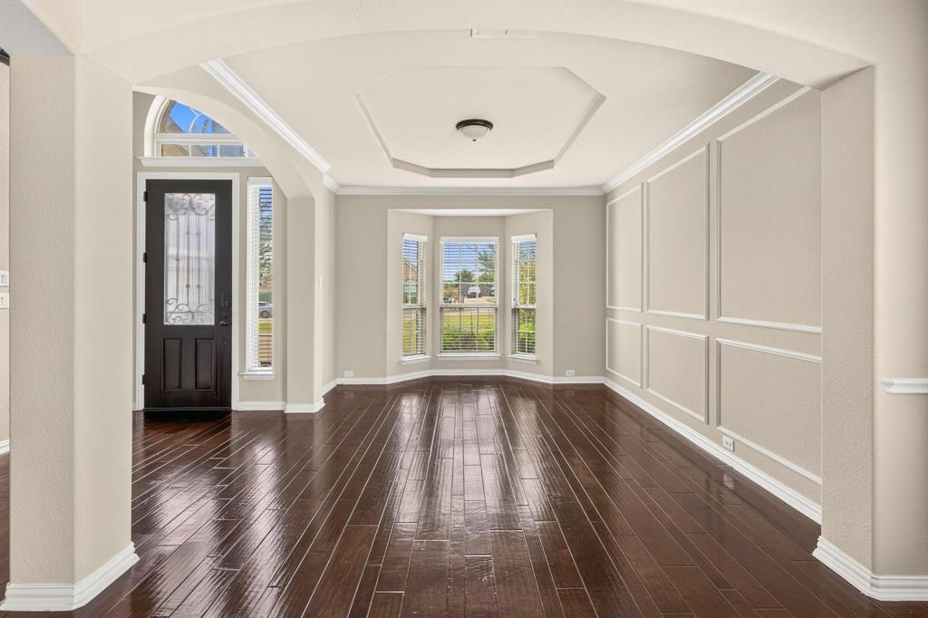 Formal dining area featuring wood-finish flooring, a tray ceiling, wainscoting, an arched entryway, and a bay window