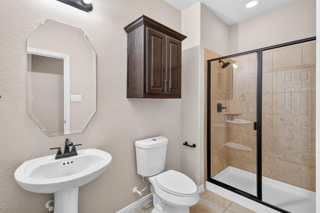 Bathroom featuring a pedestal sink with a matte black faucet, wall-mounted dark wood cabinetry, an octagonal mirror, and a walk-in shower with tiled surround and black-framed glass enclosure