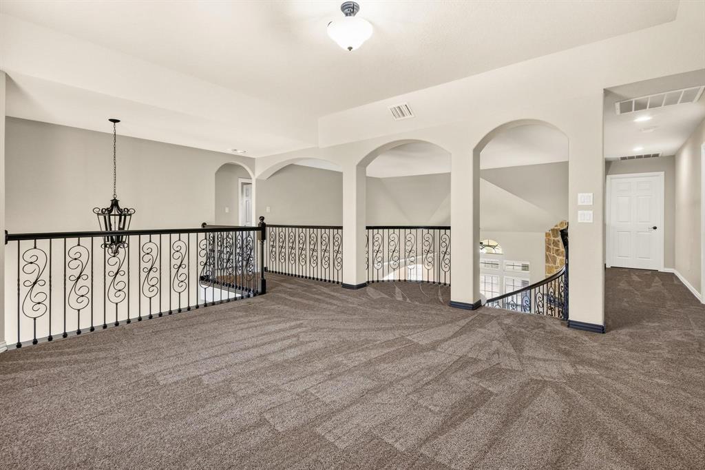 Open landing featuring decorative metal scrollwork railings, arched architectural detailing, wall-to-wall carpeting, and hanging pendant lighting
