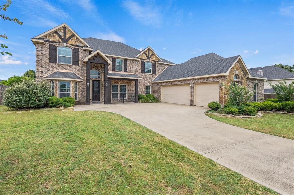 Two-story brick exterior featuring timber-accented gables, a covered entryway, multi-pane windows with decorative shutters, and a three-car garage
