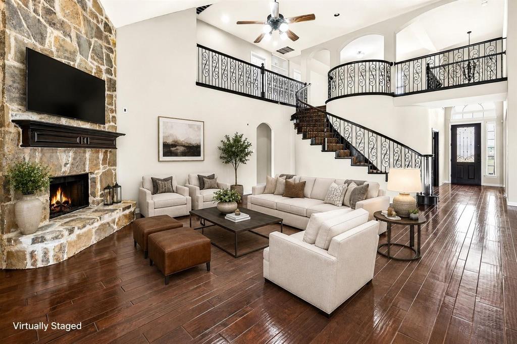 High-ceilinged living area featuring a floor-to-ceiling stone fireplace, wood-finish flooring, curved staircase with ornamental metal railing, and arched architectural detailing