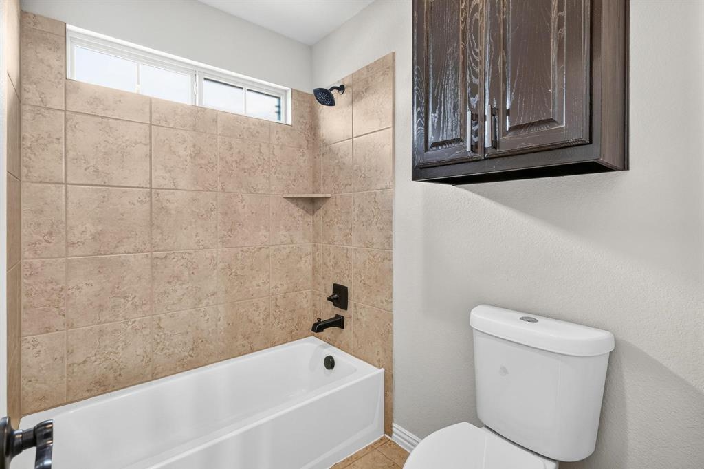 Bathroom featuring a shower-tub combination with tan ceramic wall tile, dark-finish hardware, built-in cabinetry, and a transom window