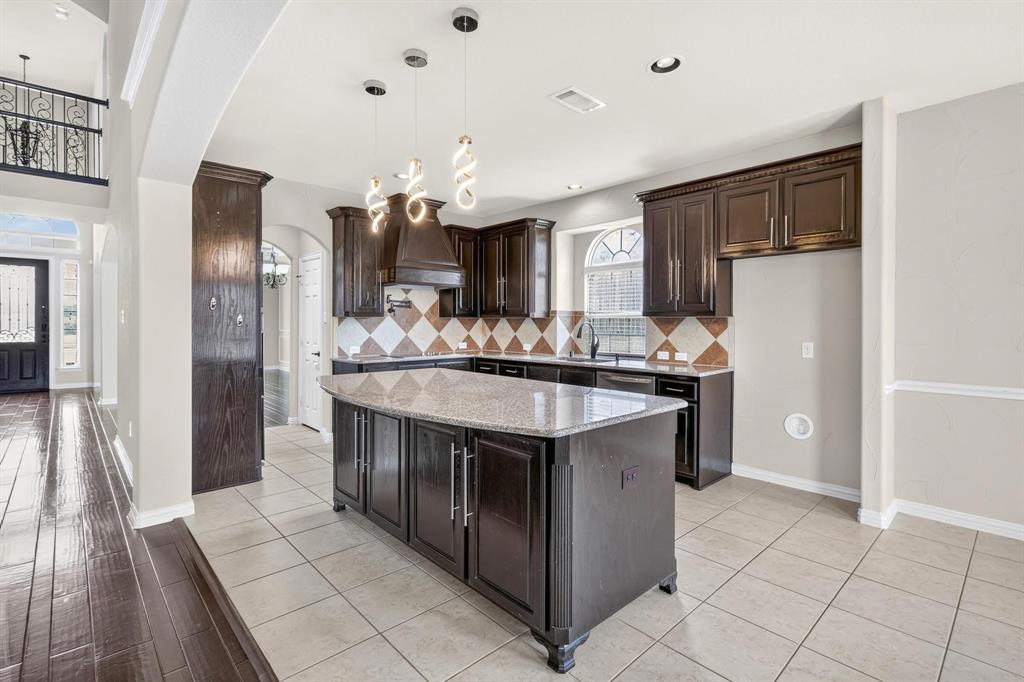 Kitchen featuring dark-finish cabinetry, central island with stone-surface countertop, decorative tile backsplash, pendant lighting, and arched window