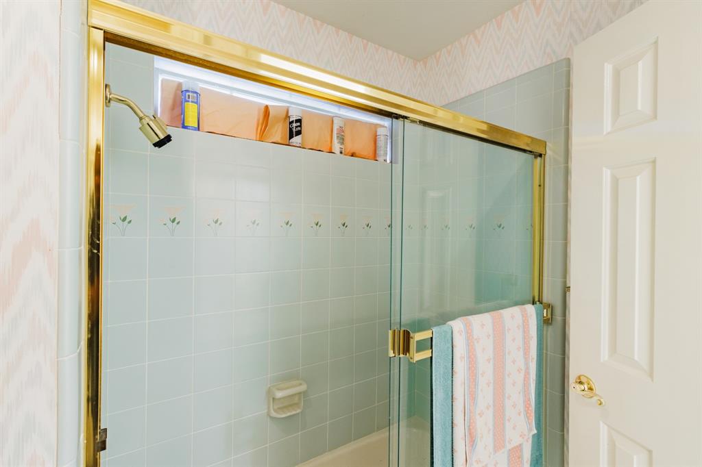Tiled shower surround with decorative floral accents, sliding glass shower door, gold-finish hardware, and transom window