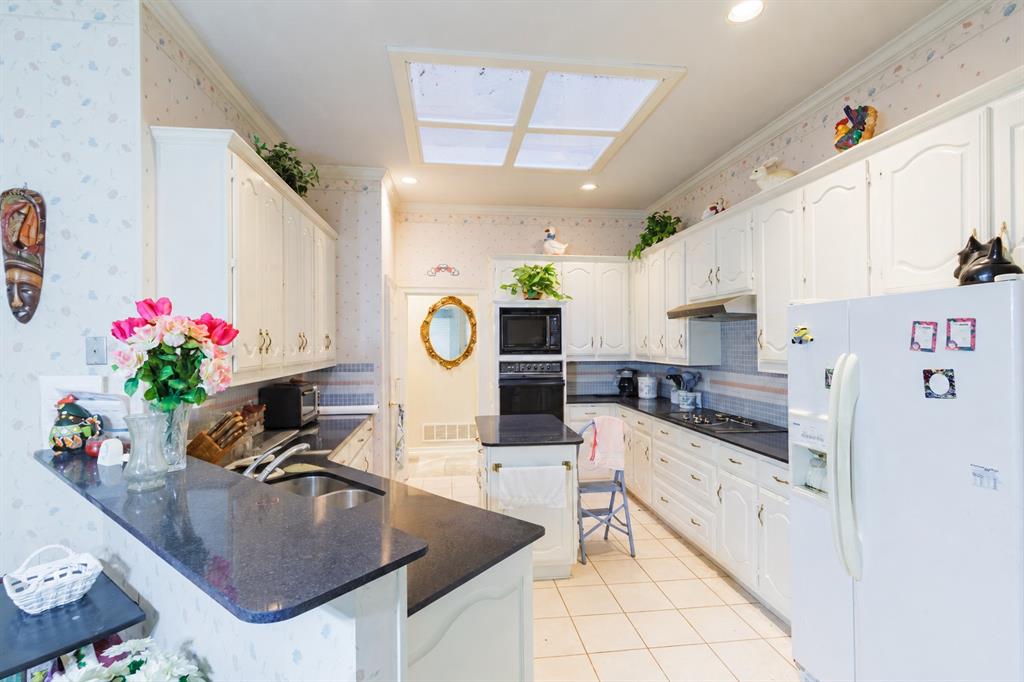 Kitchen featuring white cabinetry, dark solid-surface countertops, built-in dual ovens, a tile floor, and a recessed skylight