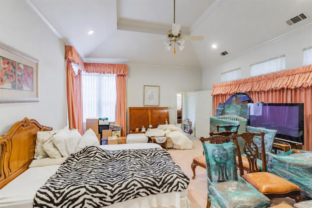 Vaulted ceiling featuring a central recessed area, multi-tiered crown molding, and a ceiling-mounted light fixture with integrated fan