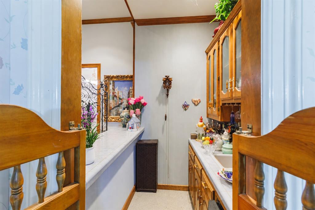 Kitchen featuring wood cabinetry with glass-front display panels, stone-finish countertops, and an integrated pass-through window with decorative wood trim