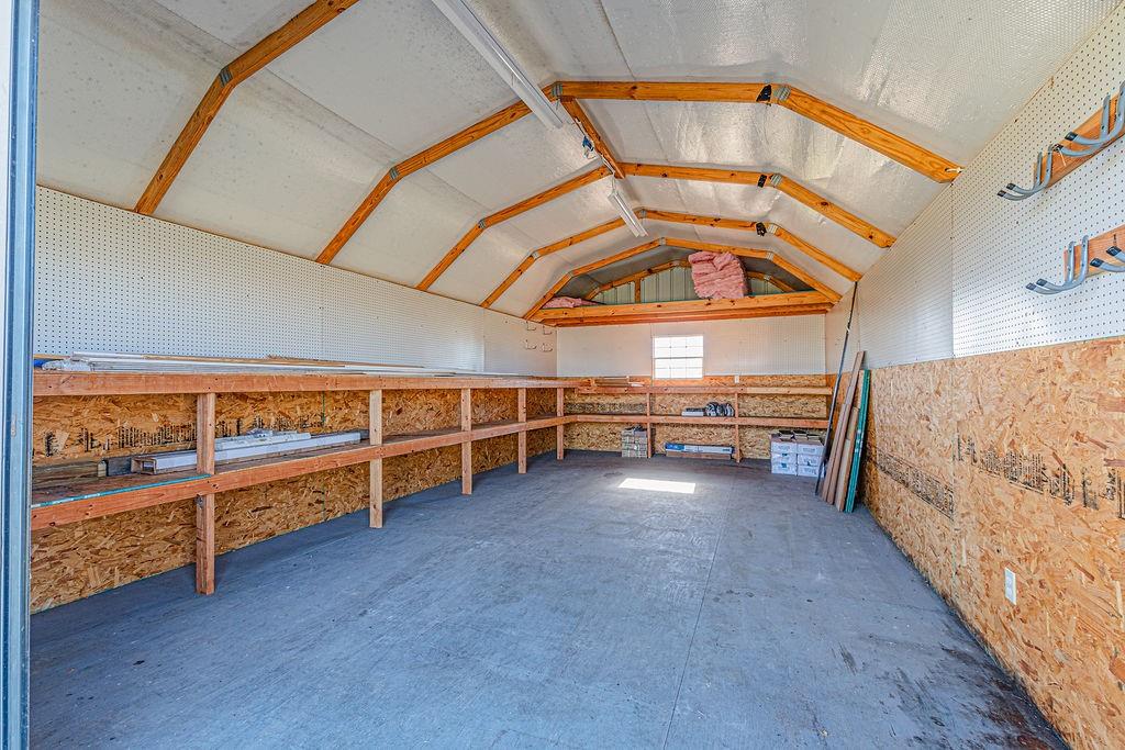 Storage structure with exposed wood framing, built-in wooden shelving, pegboard wall panels, and interior task lighting