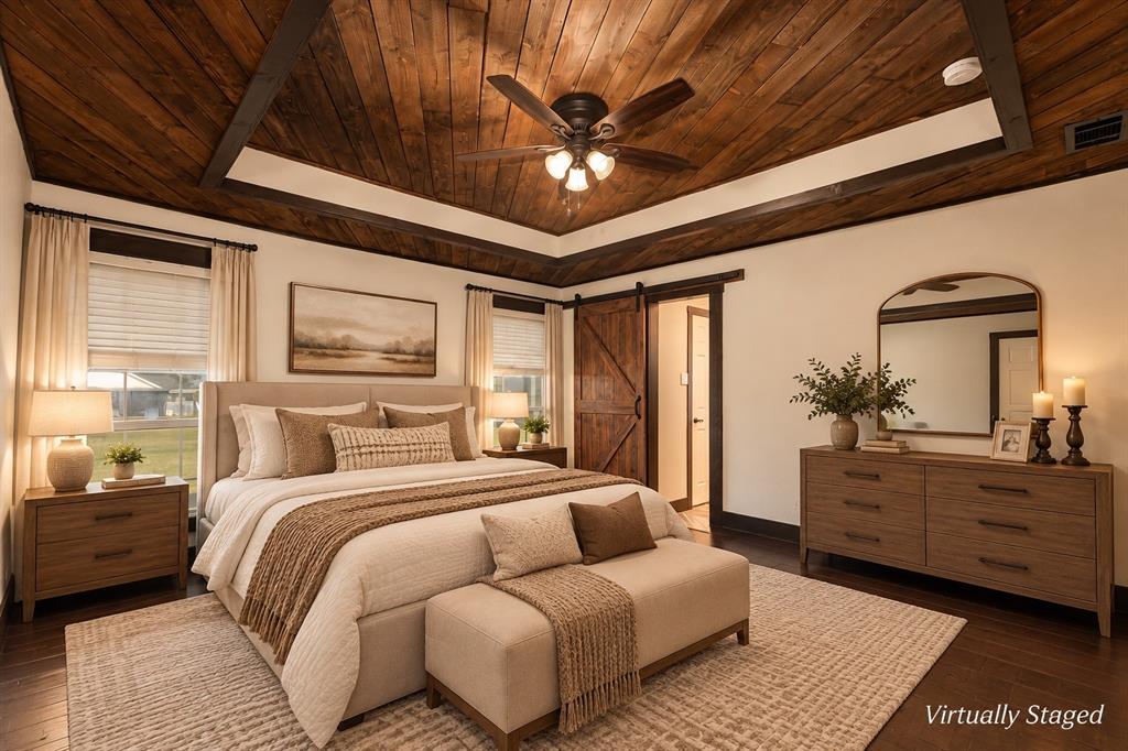 Tray ceiling with natural wood-finish planking, dark timber crown molding, integrated ceiling fan, and sliding barn-style door