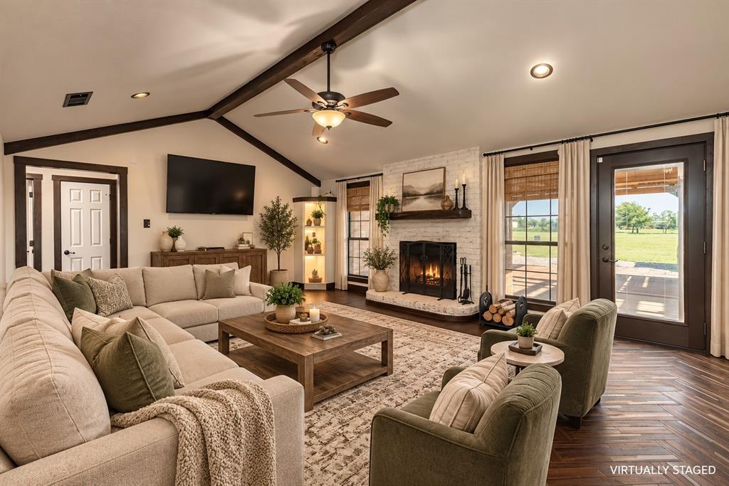 Vaulted ceiling featuring exposed beams, masonry fireplace with a wood mantel, wood-finish flooring, and built-in corner cabinetry with integrated lighting