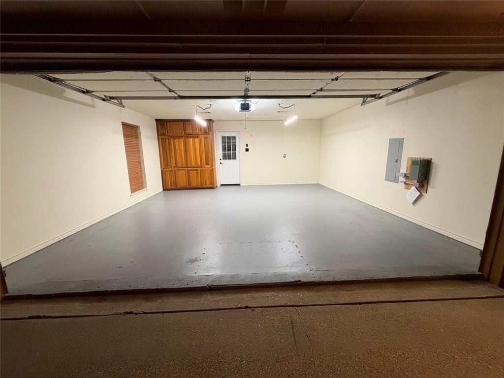 Attached garage featuring a smooth-finished floor, built-in wooden cabinetry, a white panel door with glass inset, and overhead lighting