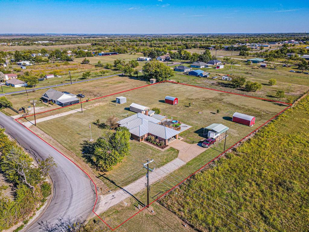 Expansive rural acreage featuring a single-story residence, multiple detached storage structures, an open-sided carport, and a paved driveway