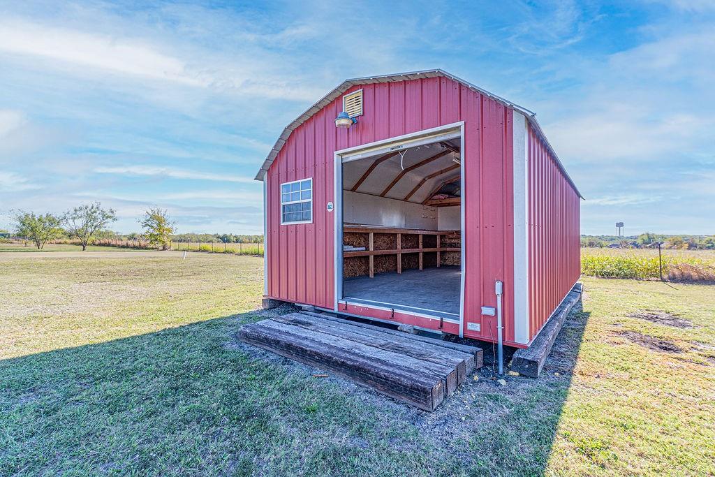 Barn-style exterior outbuilding featuring metal siding, a wide-opening entrance, built-in wooden shelving, and timber-frame foundation supports