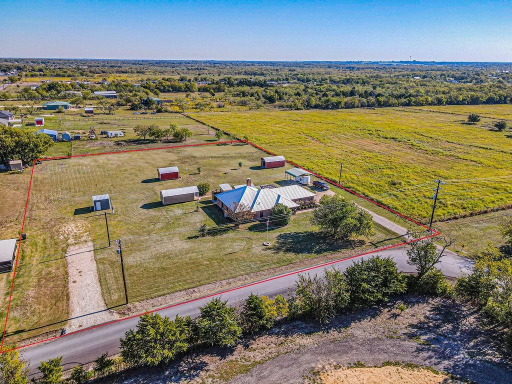 Expansive acreage featuring a detached metal structure, multiple outbuildings, a gravel driveway, and a residential building with a metal roof