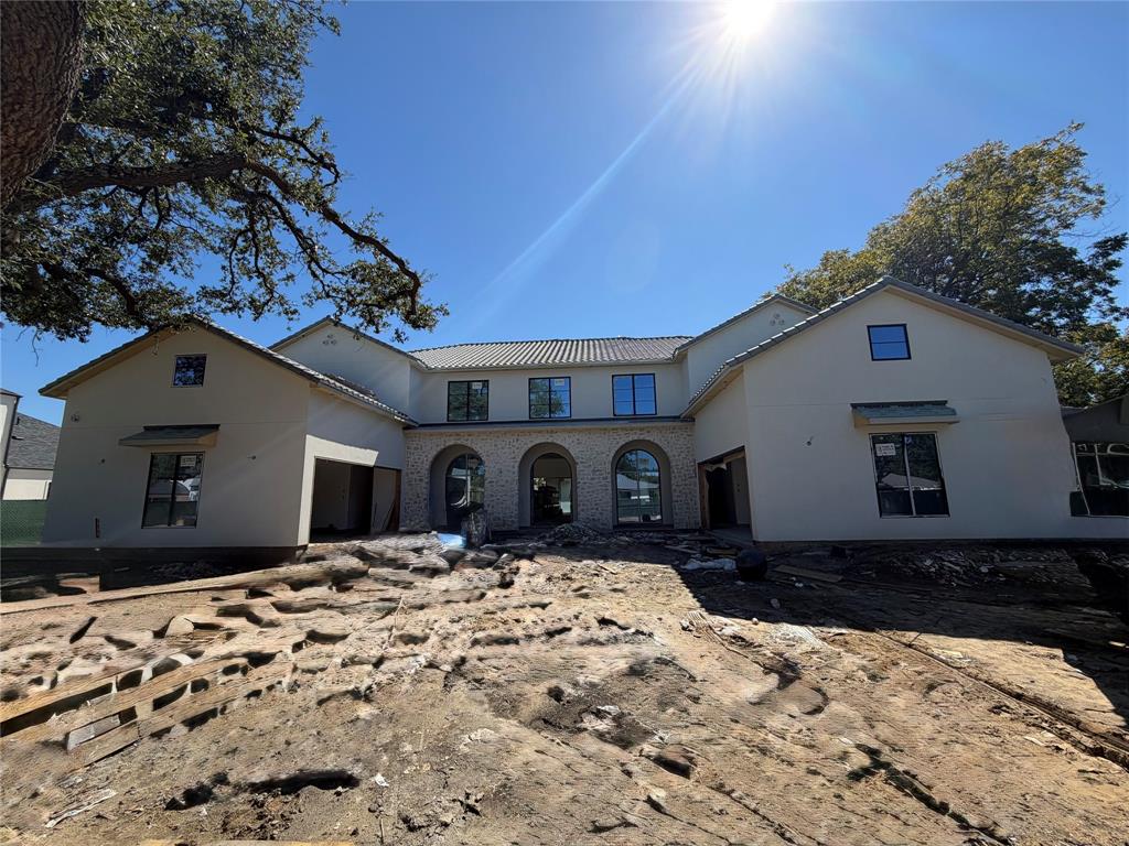 Stucco exterior featuring Stoned arched masonry detailing, a metal roof, and dark-framed windows