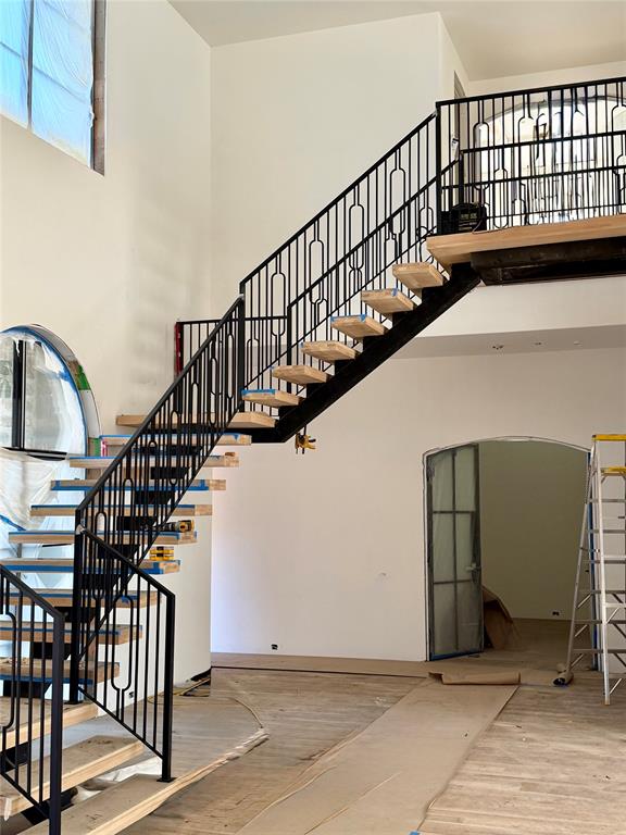 Open-riser staircase featuring natural wood treads and a geometric black metal railing, complemented by an arched window and a matching arched interior doorway