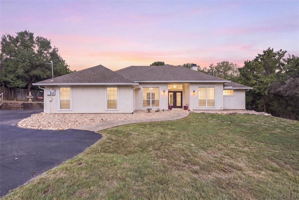Single-story stucco exterior featuring a multi-gabled roofline, asphalt driveway, stone landscaping, and grid-pattern windows