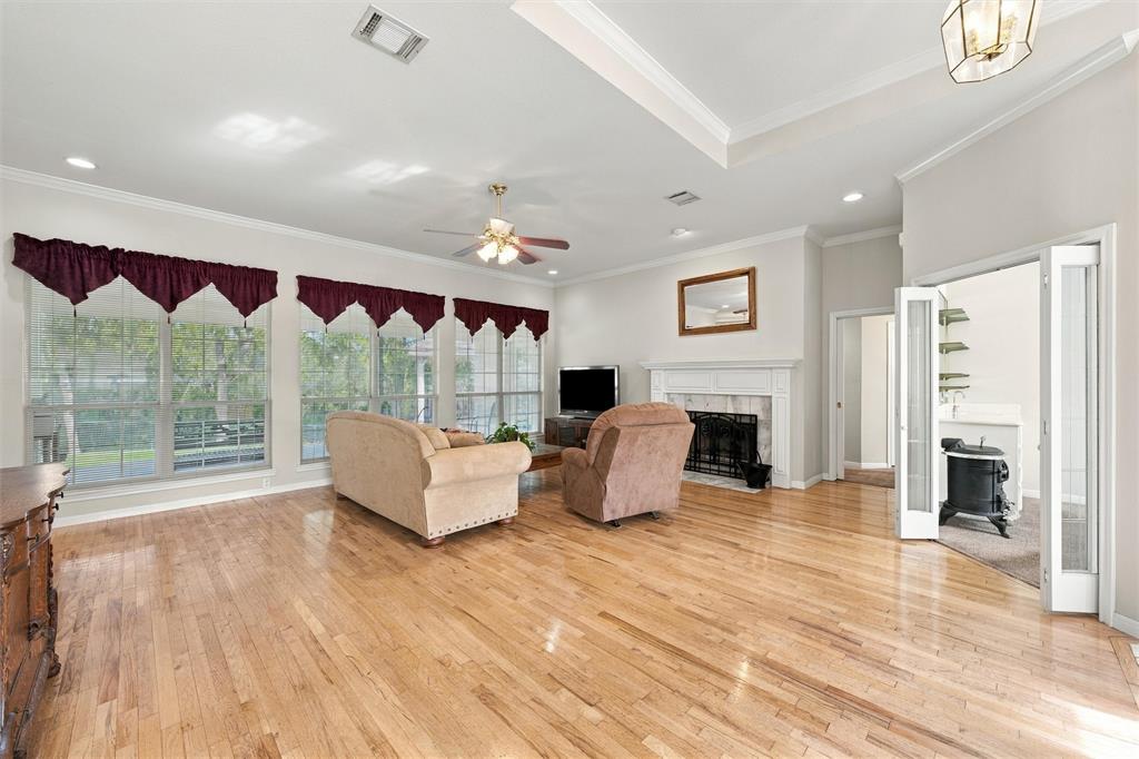 Living area featuring wood-finish flooring, tray ceiling, fireplace with detailed mantel, recessed lighting, and large windows with natural illumination