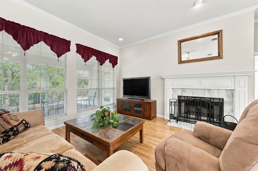 Living area featuring wood-finish flooring, floor-to-ceiling windows, and a fireplace with a white mantel and stone surround
