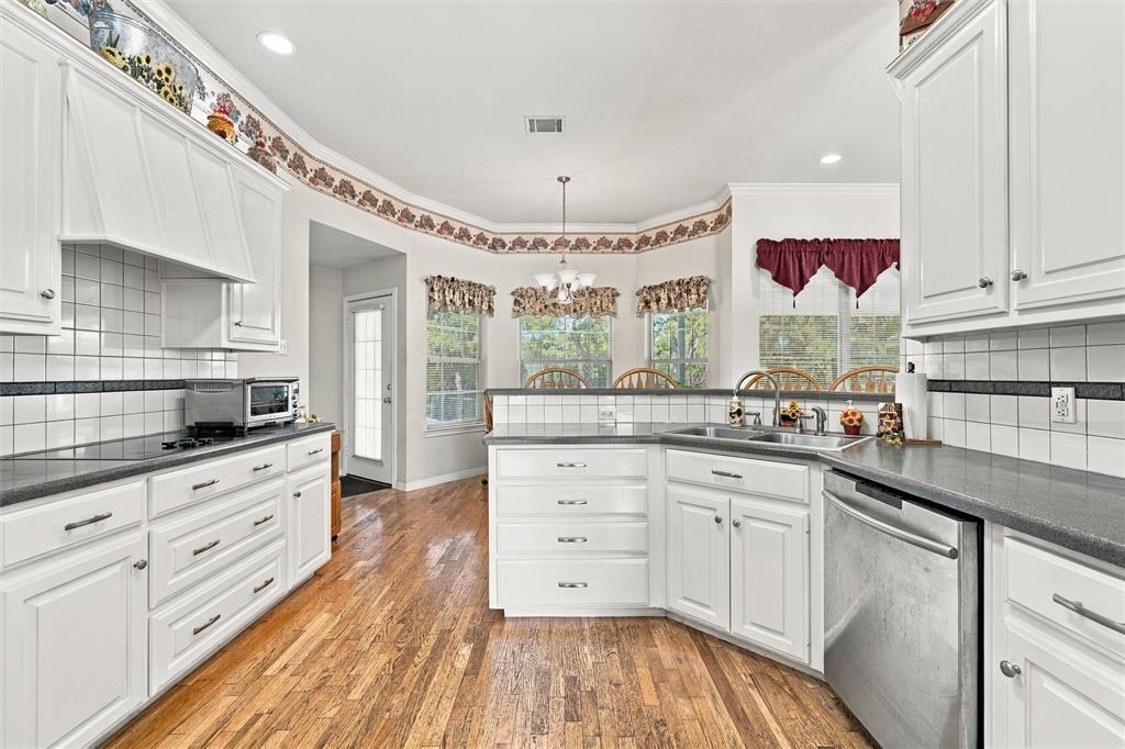 Kitchen featuring white shaker-style cabinetry, dark solid-surface countertops, square tile backsplash with decorative accents, wood-finish flooring, and recessed lighting