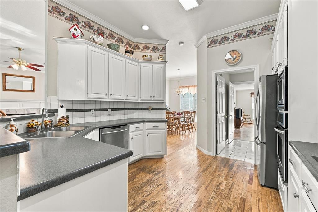 Kitchen featuring white cabinetry, solid-surface countertops, tile backsplash, wood-finish flooring, and built-in stainless steel double wall ovens