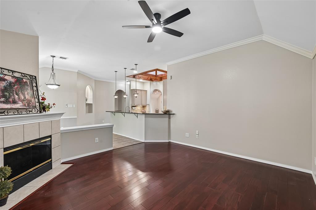 Vaulted ceilings, wood-finish flooring, tiled fireplace surround, integrated kitchen breakfast bar, and pendant lighting