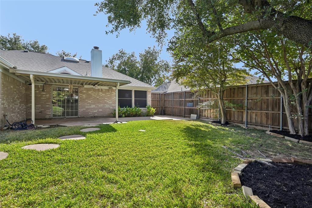Brick exterior with a covered patio, stone garden edging, wood privacy fencing, and mature trees