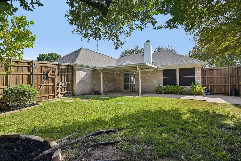 Brick exterior featuring a covered patio, fenced yard, and stone-bordered landscaping