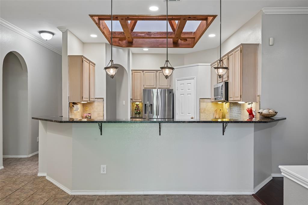 Kitchen featuring an expansive breakfast bar with a ceiling-mounted skylight with wood framing, recessed lighting, and stainless steel appliances