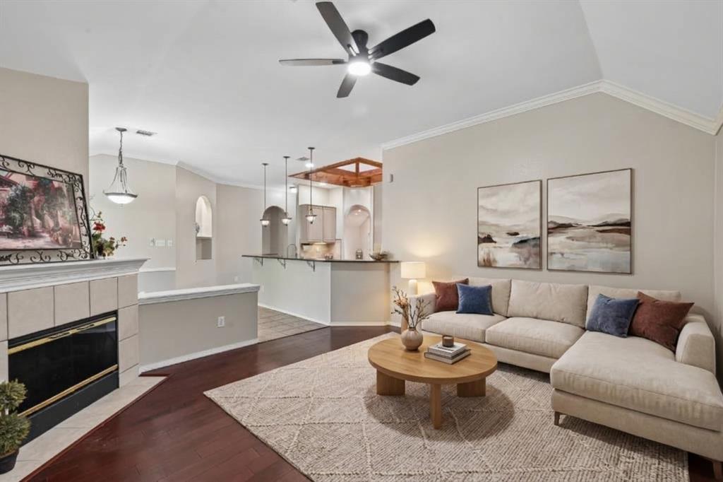 Vaulted ceilings with a central ceiling fan, fireplace with tile surround, wood-finish flooring, and arched architectural details