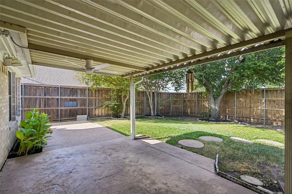 Covered patio featuring a corrugated metal roof and ceiling fan, stamped concrete flooring, fenced backyard, and mature trees