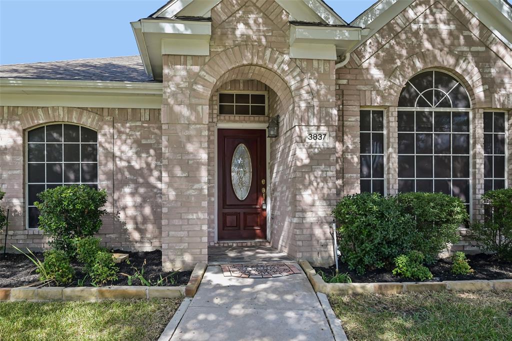 Brick facade entry featuring an arched stone portico, a wood-finish front door with an oval glass insert, a transom window, and expansive grid-pane windows
