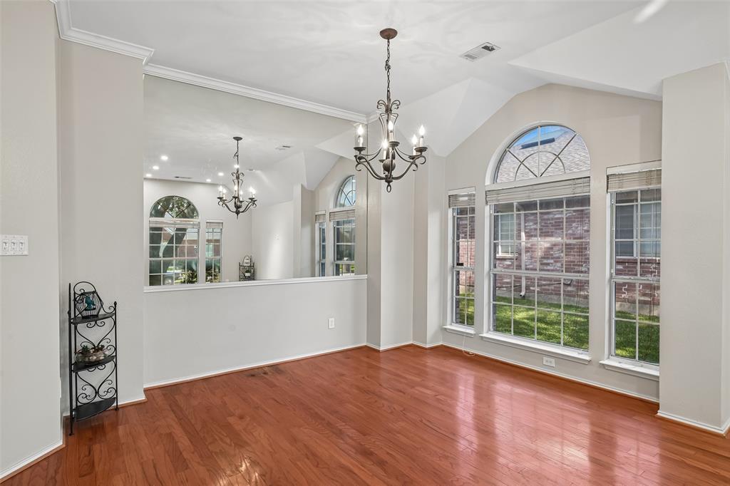 Vaulted ceilings with an expansive wall mirror, wood-finish flooring, multi-pane arched windows, and a decorative metal chandelier