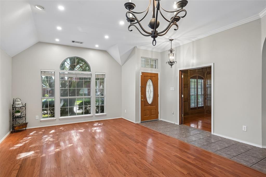 Vaulted ceilings featuring recessed lighting, wood-finish flooring, an arched window, a solid wood entry door with an oval glass insert, and a decorative wrought iron chandelier