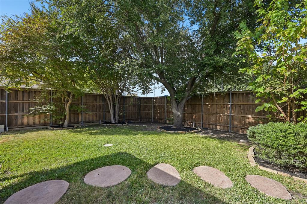 Backyard featuring mature trees, wood privacy fencing, a manicured lawn, and stone paver path