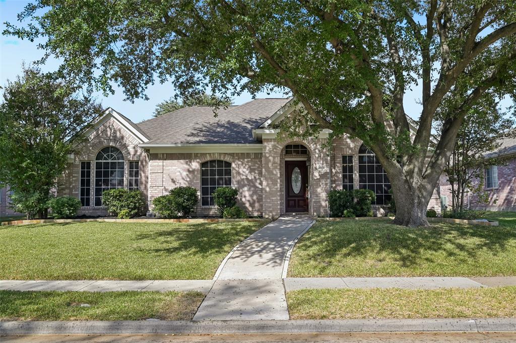 Single-story brick exterior featuring an arched entryway, decorative oval-glass front door, grid-pattern windows, and mature trees