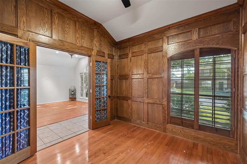 Custom wood paneling, wood-finish flooring, vaulted ceiling, arched window with wood trim, and glass-paneled double doors