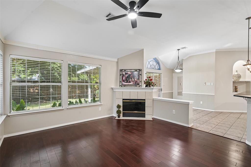 Vaulted ceilings, wood-finish flooring, corner fireplace with tile surround, large dual-pane windows, and arched architectural niche